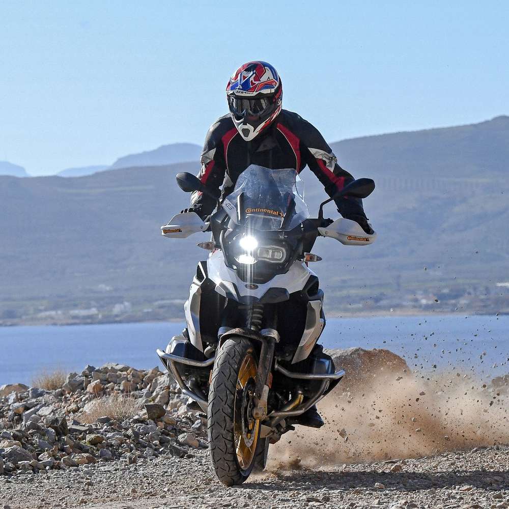 BMW GS Motorrad driftet von rechts nach links. Hinter dem Hinterrad fliegt der Schotter.