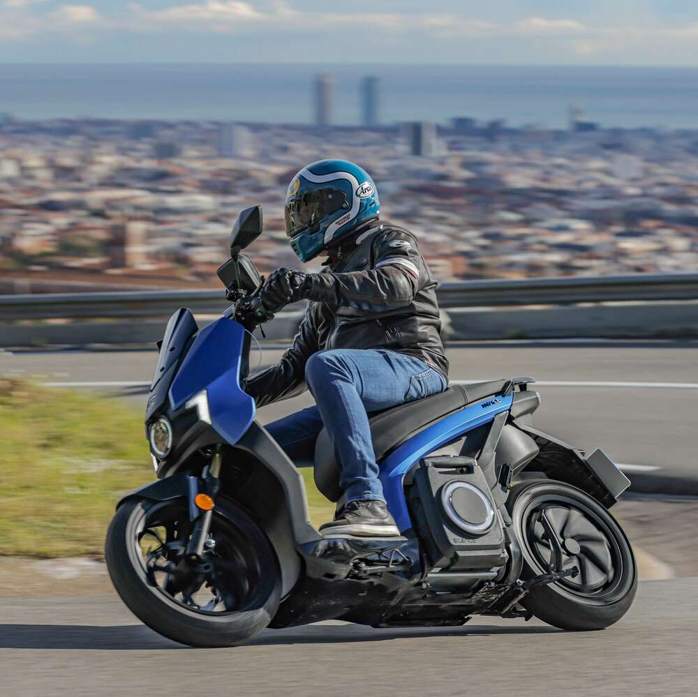 Seat Mó eScooter 125 Performance in Blau fahrend in der Kurve schräg von vorne