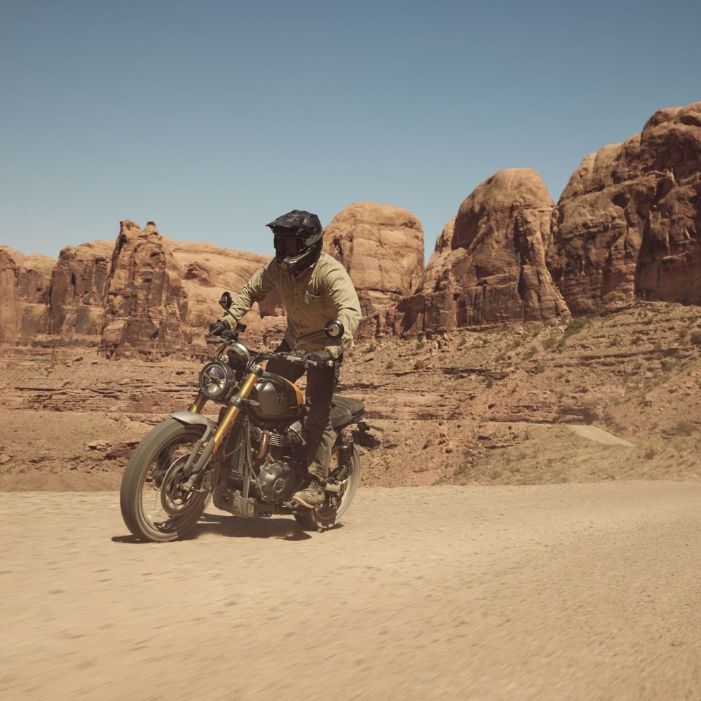 Triumph Scrambler 900 Modelljahr 2026 in Grau und Gelb fahrend auf Sand